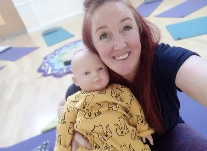 Em smiling at camera and holding a doll used in her classes